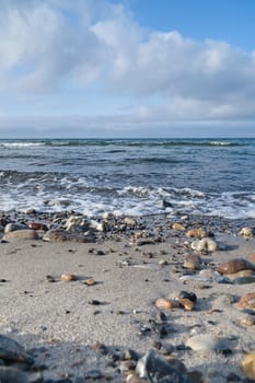 Stone beach on the coast of Denmark. Stones in the sand and in the water. Landscape photo from sea