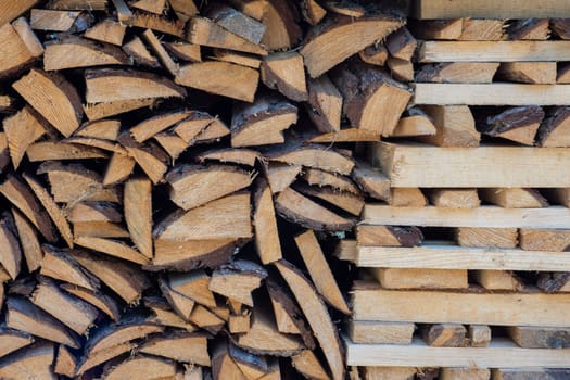 A stack of chopped firewood and logs arranged in neat rows for drying and storage. The various wood textures against a sunny day.