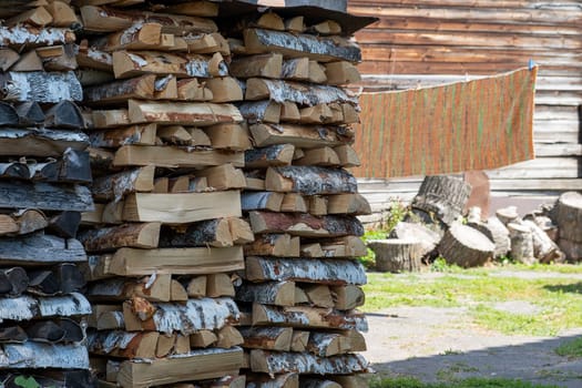 A woodpile of firewood in a rural area, against a village yard on a sunny summer day. Selective focus.