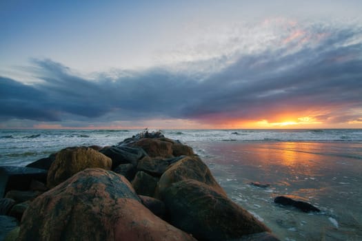 Sunset on the beach in Denmark. Stone groyne in the foreground. Walk on the coast in the sand. Landscape photo by the sea