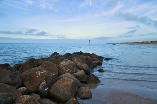 Stone groyne juts out into the water off the coast in Denmark. Sunny day. Landscape photo by the sea