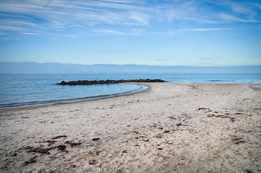 Sandy beach on the coast of Denmark. Stone groyne in the bay, sunshine while walking. Landscape photo by the sea