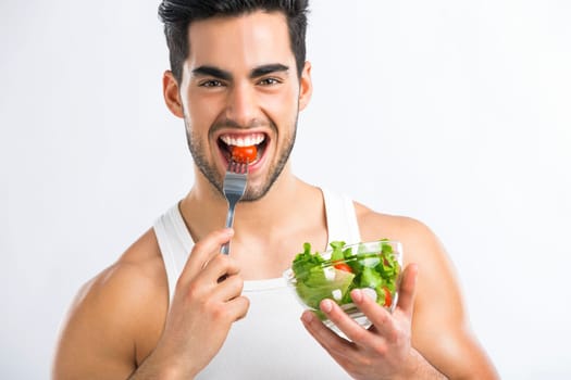 Handsome young man eating a healthy salad, isolated over a gray background