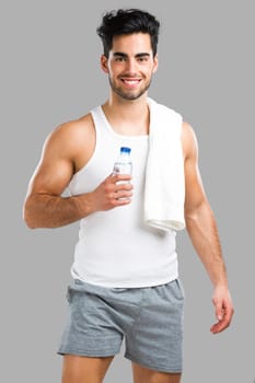 Portrait of a athletic young man drinking water, isolated over a gray background
