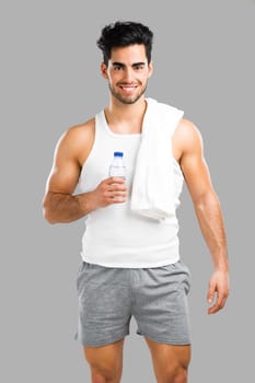 Portrait of a athletic young man drinking water, isolated over a gray background