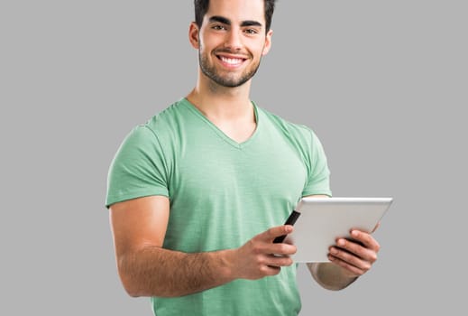 Handsome young man working with a tablet, isolated over gray background
