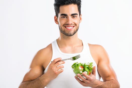 Handsome young man eating a healthy salad, isolated over a gray background