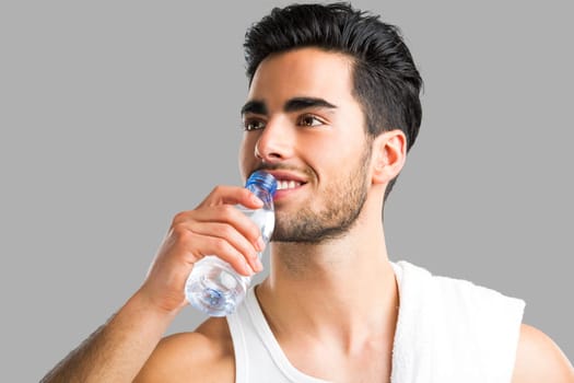 Portrait of a athletic young man drinking water, isolated over a gray background