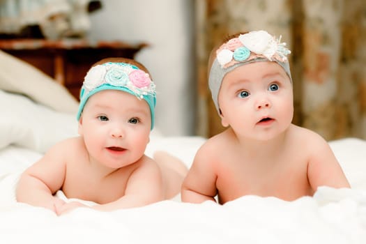 Two twin babies, seven-month girls in nice headbands in bed on white sheets