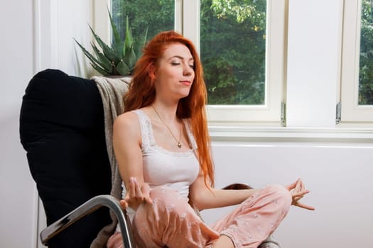 Young woman with long red hair sits in an armchair and reads a book