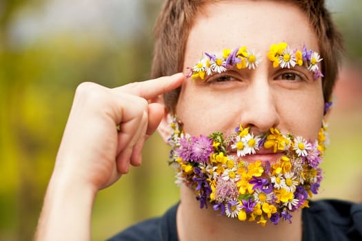 young hipster man face-covered with flowers makes an hand gesture meaning he wants you to think about environment and green power