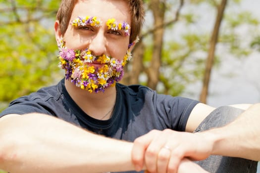 young self-confident man looking at camera with his eyebrow and beard disguised with flowers