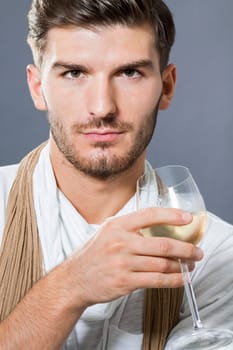 attractive young man with elegant swearing and scarf with a wine glass in his hand against a grey background
