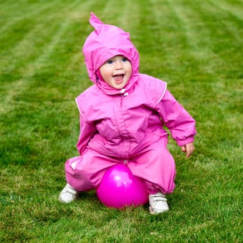 Cute little baby girl wearing pink suit playing with pink ball on a lawn