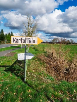 Landscape view with a sign for direct potato sales on a country road in East Friesland with a blue sky and large white clouds.