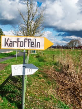 Landscape view with a sign for direct potato sales on a country road in East Friesland with a blue sky and large white clouds.