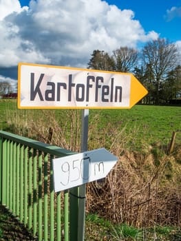 Information sign for direct potato sales on a country road in East Friesland with a blue sky and large white clouds.