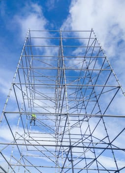 Unidentified worker at height dismantling a scaffolding tower. Blue cloudy sky on background