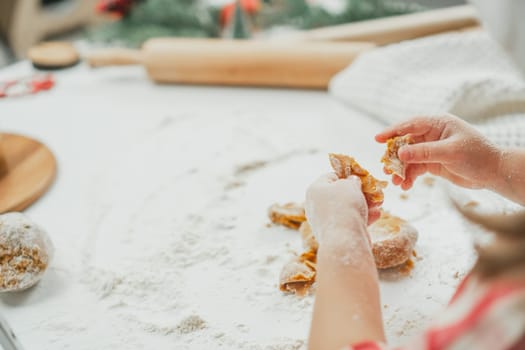 Partially blurred hands of little girl in red checkered shirt prepare dough for gingerbread cookies in white kitchen. Child knead dough on white table strewn with flour