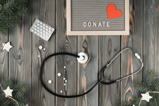 Medical stethoscope with pills on gray wooden table, top view. Social helping sick. Medicine and treatment. Decoration from spruce branches. Giving money. New Year or Christmas charity, kind heart.