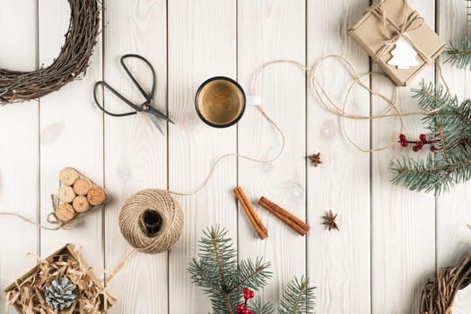 Handmade gift box in festive package decorated with postcard, top view. Spruce branches, cinnamon, cup of coffee and tools. Crafting present. Objects layout. Christmas or New Year holiday concept.