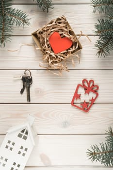 Mini model of house, keys and present box with red paper heart postcard, top view. Frame from decorative spruce branches. Buying new real estate. Accommodation as gift. Christmas or New Year holiday.