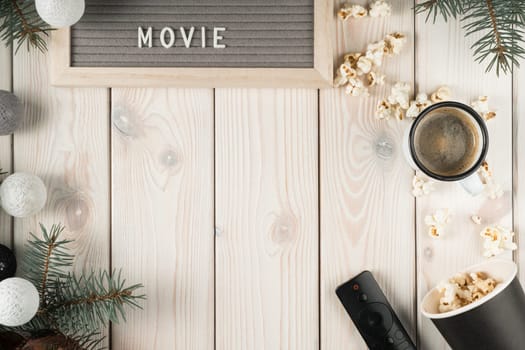 Watching movie film at home on TV with cup of coffee and popcorn, top view. Decorative spruce branches and christmas tree balls. White planking. Objects layout. Christmas or New Year holiday concept.