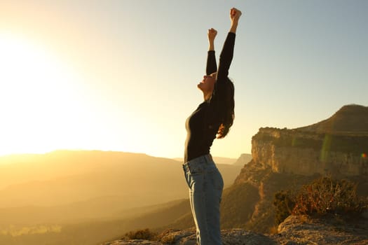 Side view portrait of an euphoric woman raising arms in the mountain at sunset