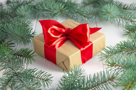 Gift wrapped in craft paper and red ribbon with green branches of a Christmas tree on a white wooden background. Merry Christmas and Happy New Year concept