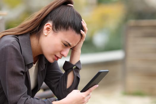 Worried teen complaining checking bad news on mobile phone in a park