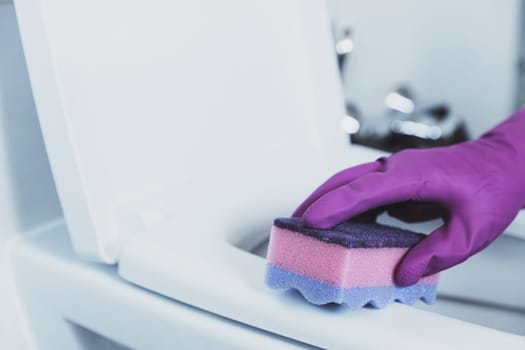 Close up on woman hand gloved in blue rubber protective gloves. Housewife cleaning toilet bowl, seat with detergent liquid, wet wipe in bathroom, restroom. Female washing, disinfecting toilet seat