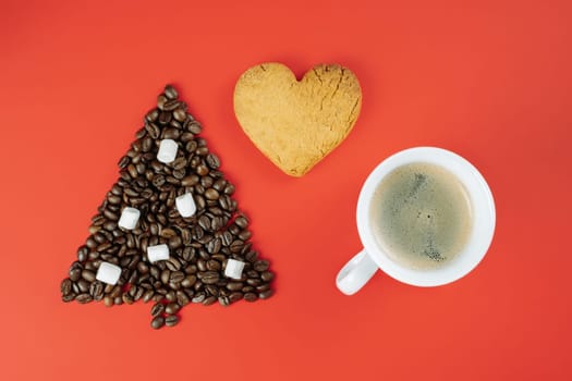 Brown coffee beans and marshmallows laid out in shape of Christmas tree with cup of coffee and heart-shaped cookie on red background. Flat lay