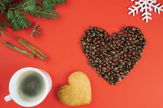Brown coffee beans laid out in shape of heart with Christmas tree branches, cup of coffee, heart-shaped cookie, cinnamon, star anise and wooden snowflake on red background. Flat lay