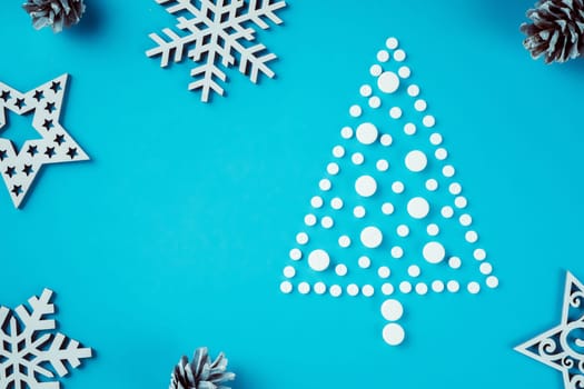 White round pills, laid out in shape of Christmas tree with wooden snowflakes and pine cones on light blue background Flat lay. Copy space