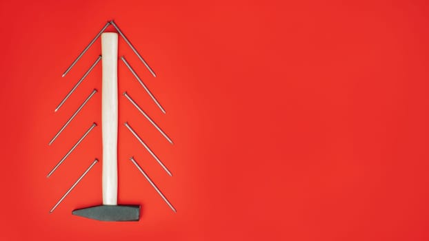 Long nails and hammer, laid out in shape of Christmas tree on red background. Banner. Flat lay. Copy space