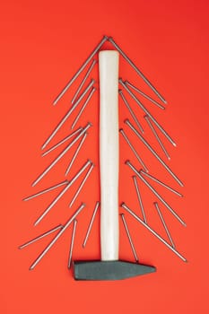 Long nails and hammer, laid out in shape of Christmas tree on red background. Vertical, flat lay