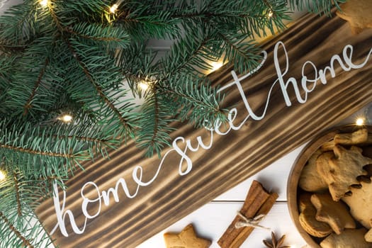 Home Sweet Home lettering burnt wood sign with gingerbread cookie, Christmas tree branches, cinnamon sticks and anise on white surface. Flat lay