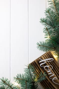 Home lettering burnt wood sign and Christmas tree branches on white wooden surface. Flat lay, copy space. Vertical