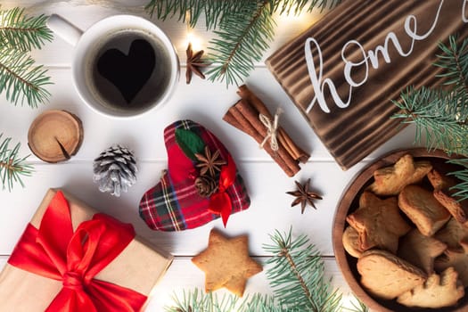 Home lettering burnt wood sign, gingerbread cookie, Christmas tree branches, cup of coffee, gift, cinnamon sticks on white surface. Flat lay