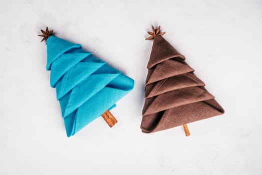 Two linen napkins folded in shape of Christmas trees on white concrete surface. New Year table setting. Top view.