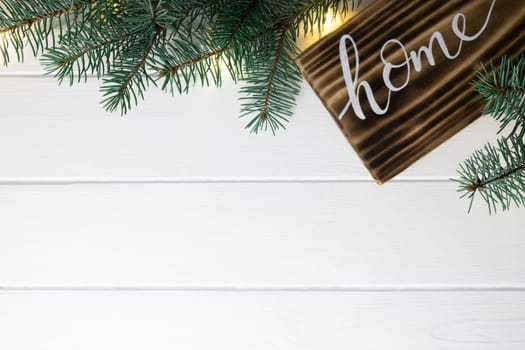Home lettering burnt wood sign and Christmas tree branches on white wooden surface. Flat lay, copy space.