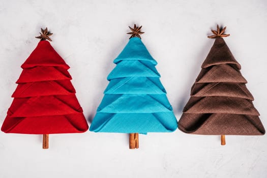 Three linen napkins folded in shape of Christmas trees on white concrete surface. New Year table setting. Top view.