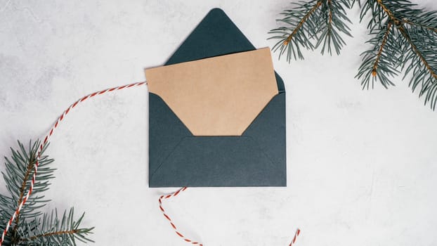 Green open envelope on white concrete background with blank kraft paper greeting card with branches of Christmas tree. New year envelope with untied cord. Copy space. Top view