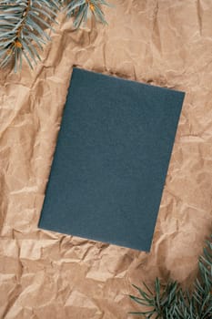 Background image of rough crumpled recycled textured kraft paper with Christmas tree branches and sheet of dark green cardboard. Top view. Copy space
