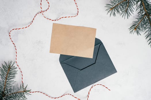 Green open envelope on white concrete background with blank kraft paper greeting card with branches of Christmas tree. New year envelope with untied cord. Copy space. Top view