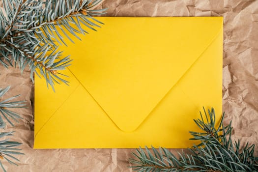 Background image of rough crumpled recycled textured kraft paper with Christmas tree branches and bright yellow cardboard envelope. Top view. Copy space