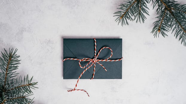 Green envelope on white concrete background with branches of Christmas tree. New year envelope tied with cord with bow. Top view