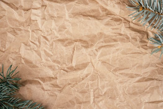 Background image of rough crumpled recycled textured kraft paper with Christmas tree branches. Top view. Copy space