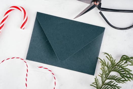 Green envelope and Christmas candy, cord, scissors on white concrete background with branch of Christmas tree. New year envelope. Top view. Copy space