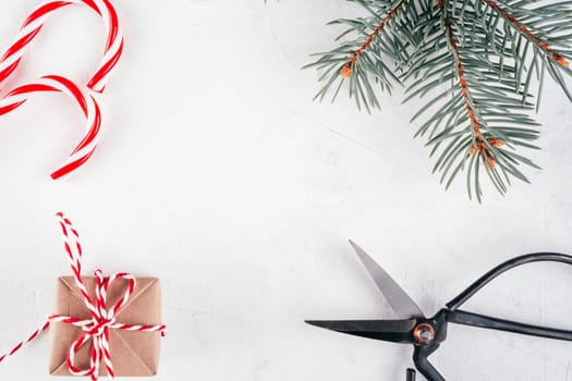 Christmas gift box and lollipop, cord, scissors on white concrete background with branch of Christmas tree. Merry Christmas and Happy New Year. Top view. Copy space